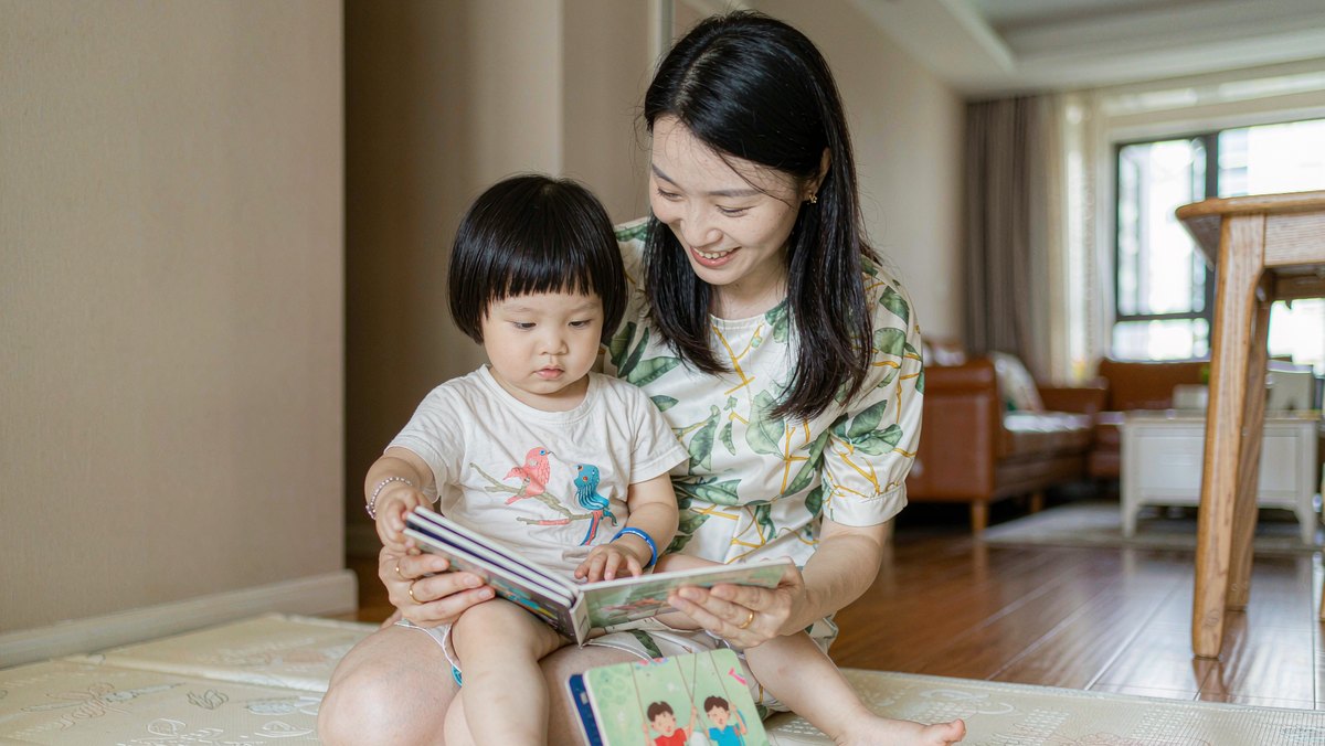 妈妈抱着幼儿一起翻硬壳纸板书