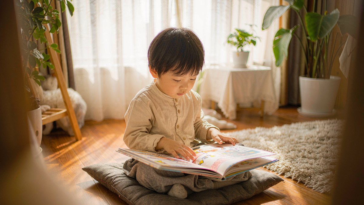 孩子坐在窗边地垫上专心翻看绘本