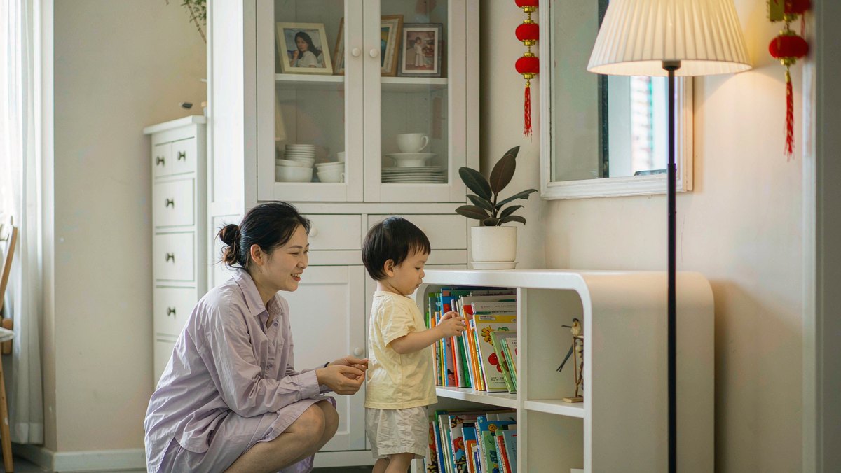妈妈蹲下和孩子一起整理低位书架上的绘本