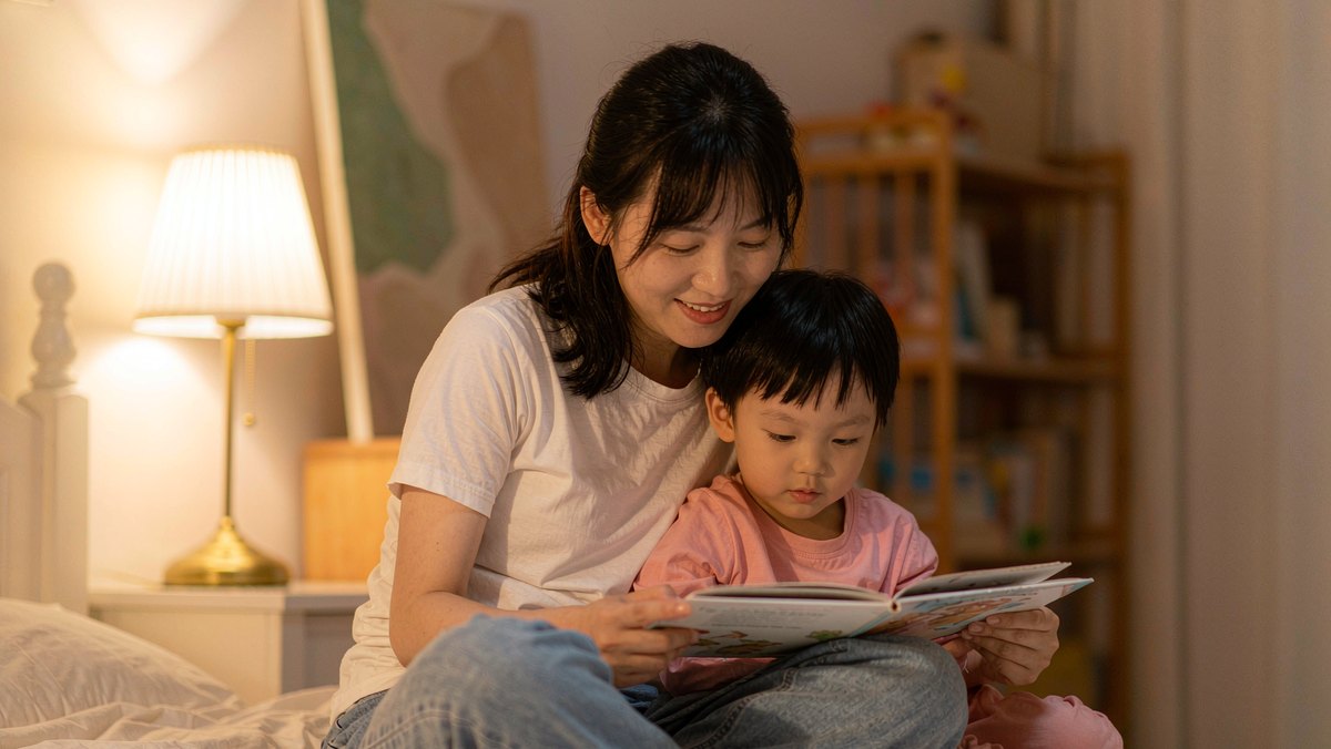 妈妈坐在床边听孩子读完一页绘本