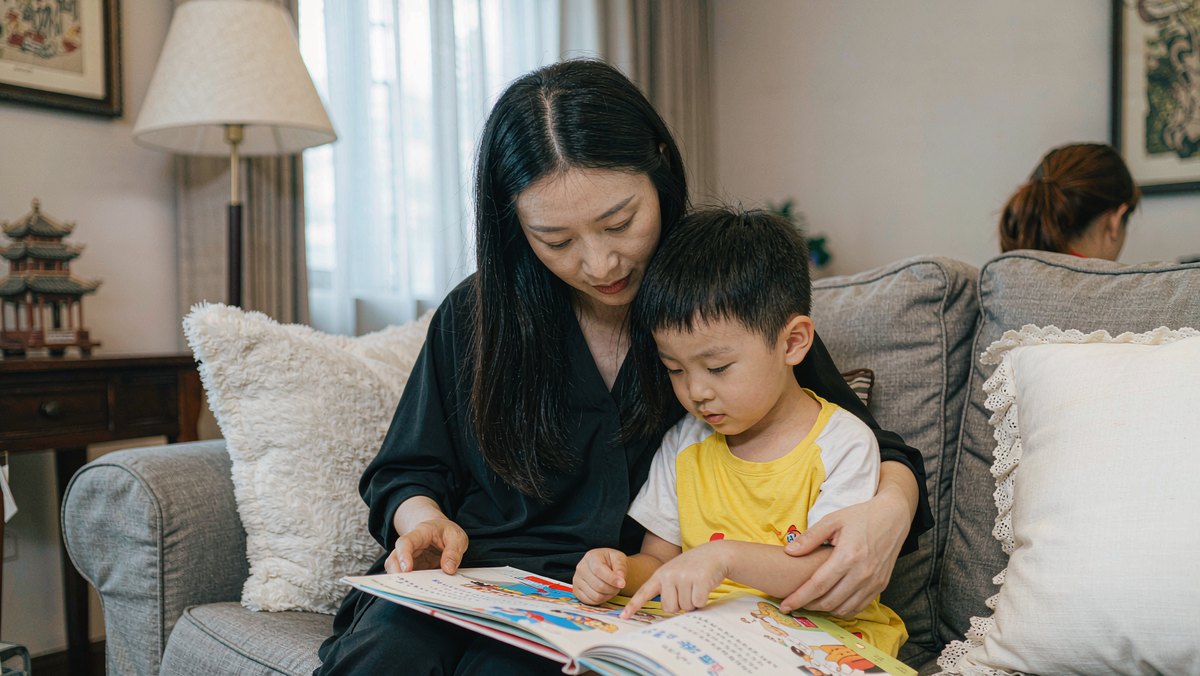 家长拿着绘本出声朗读，孩子在旁边听