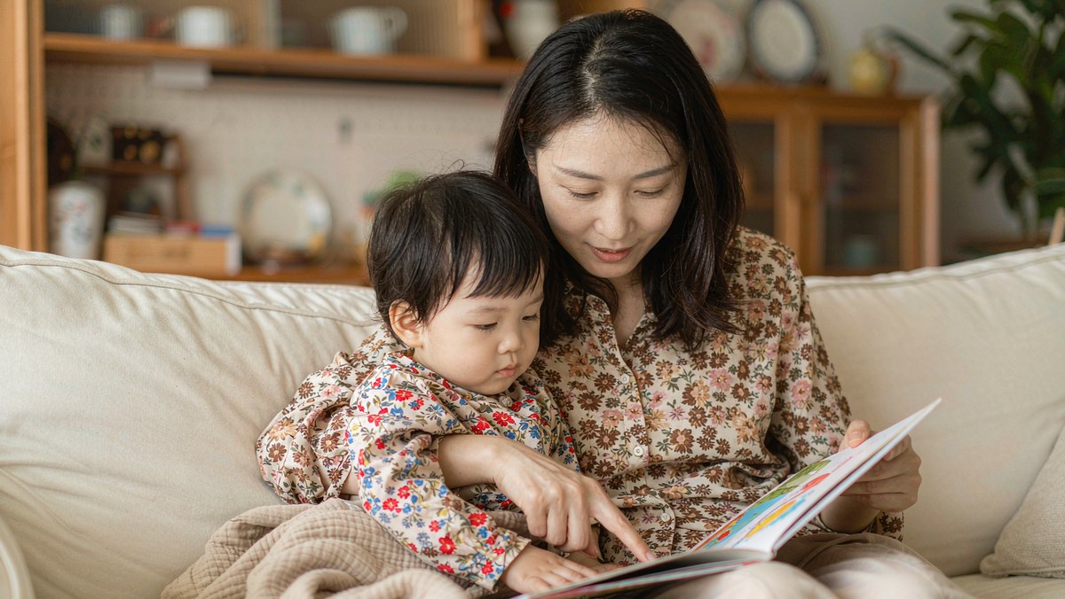 妈妈用手指着绘本上的字,孩子靠在她身边听