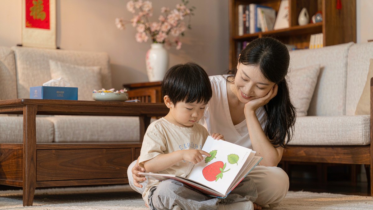 孩子自己用手指着绘本念字,妈妈在旁边微笑看着