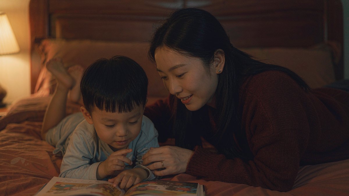 灯光柔和的卧室里,妈妈躺在床上给孩子读睡前绘本