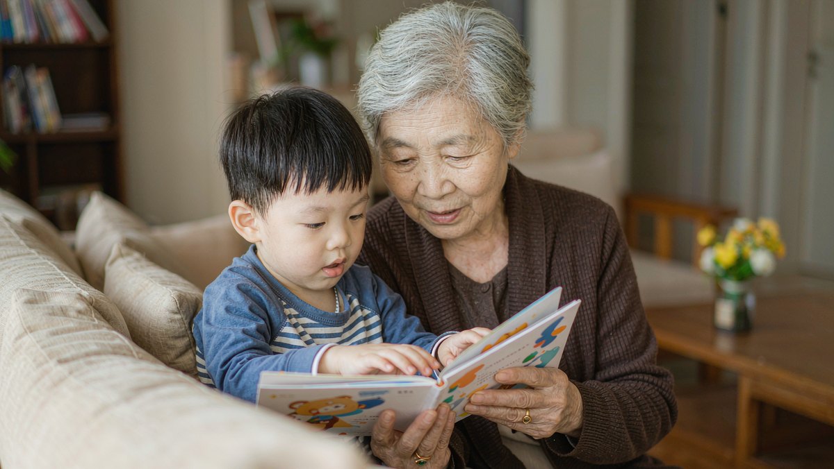 奶奶在沙发上给孙子读绘本,孩子靠在她身上
