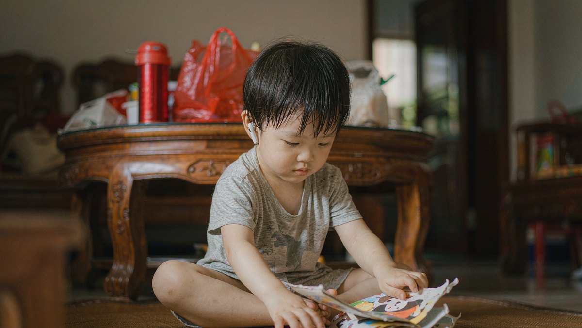 孩子坐在垫子上翻绘本,手里拿着撕坏的书页