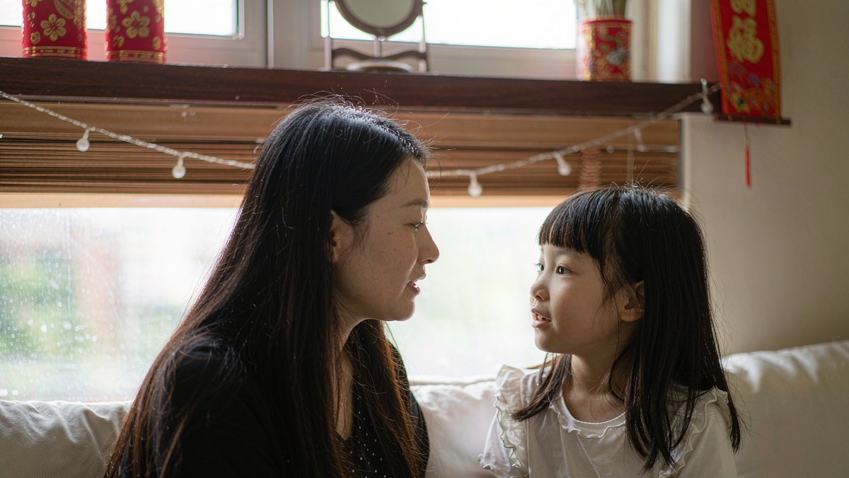 妈妈和女儿并肩坐在窗边聊着绘本里的故事