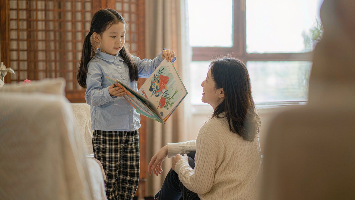 孩子在客厅给妈妈讲故事，手里举着绘本