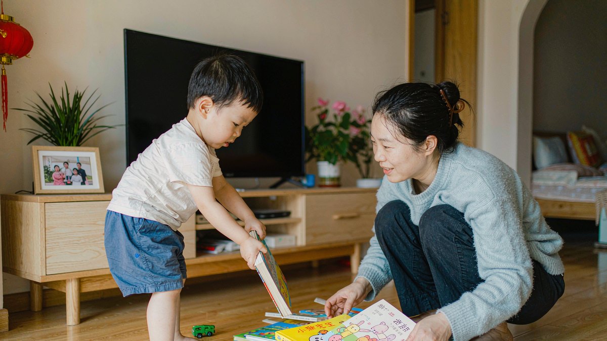 学步期幼儿把厚纸板绘本翻得乱七八糟，妈妈在旁边收拾