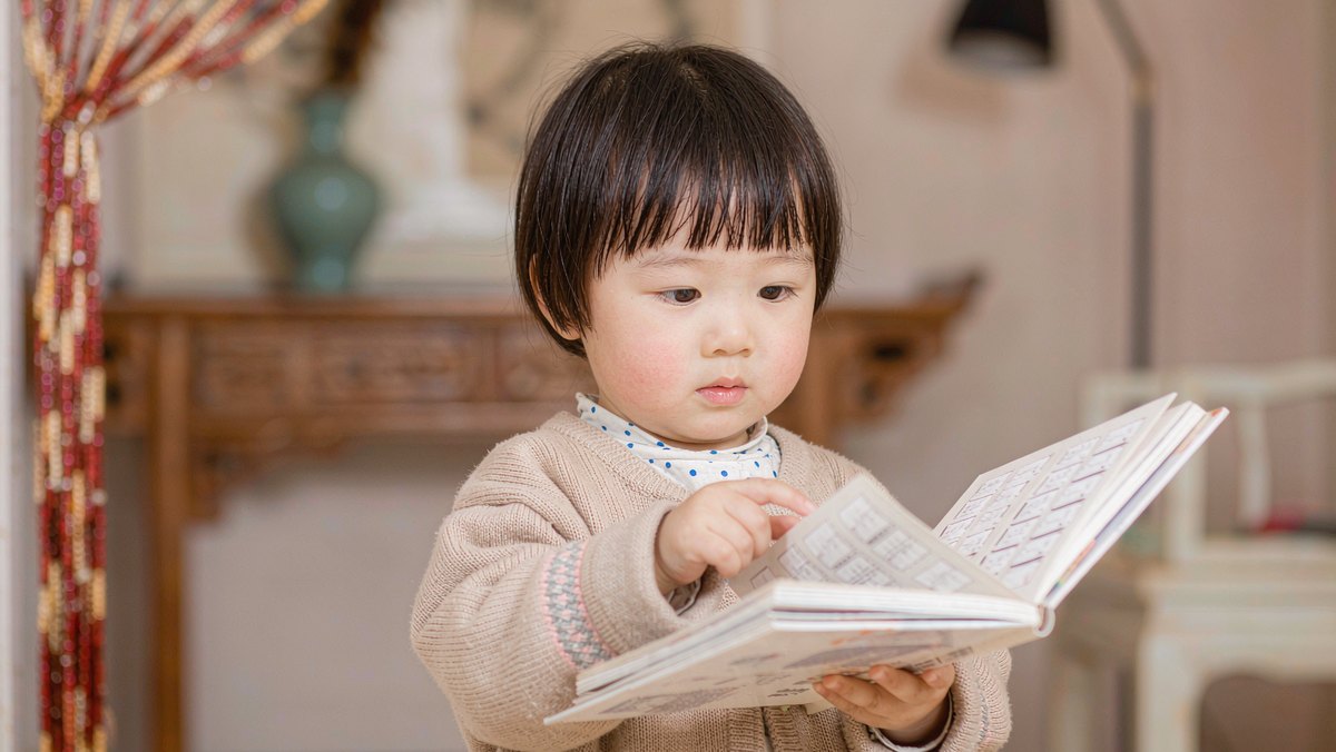 两岁半小女孩抱着一本书小心地翻，神情很爱护