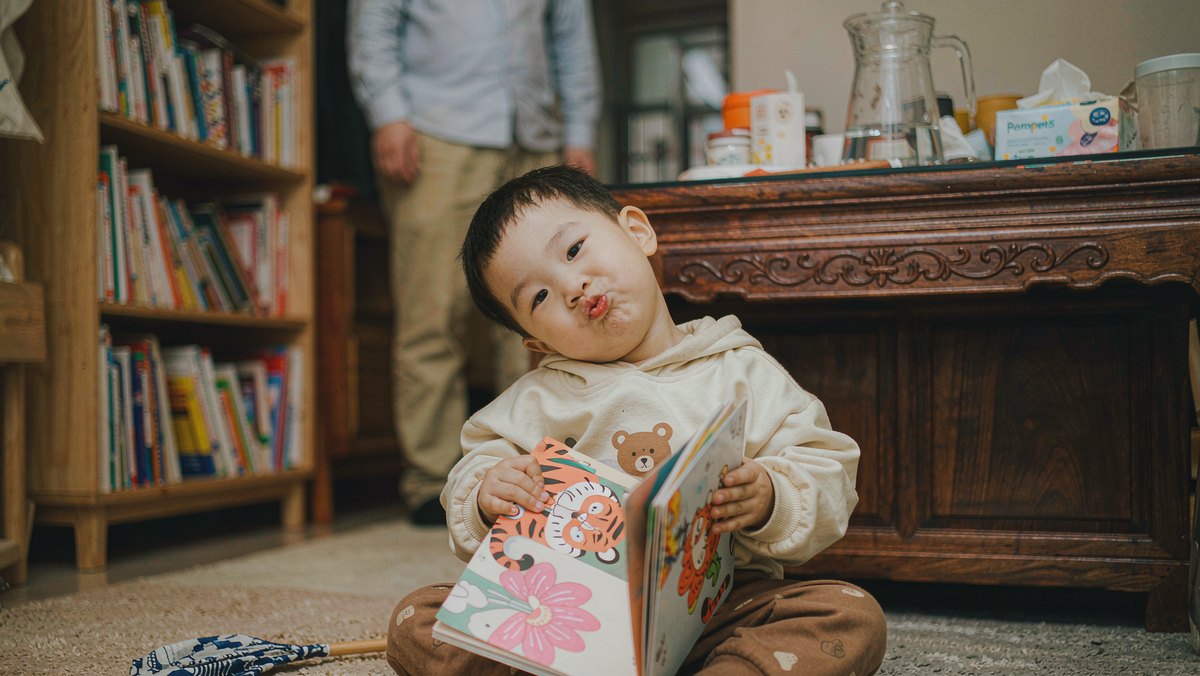 孩子坐在地毯上捧着绘本,模仿书上动物的表情