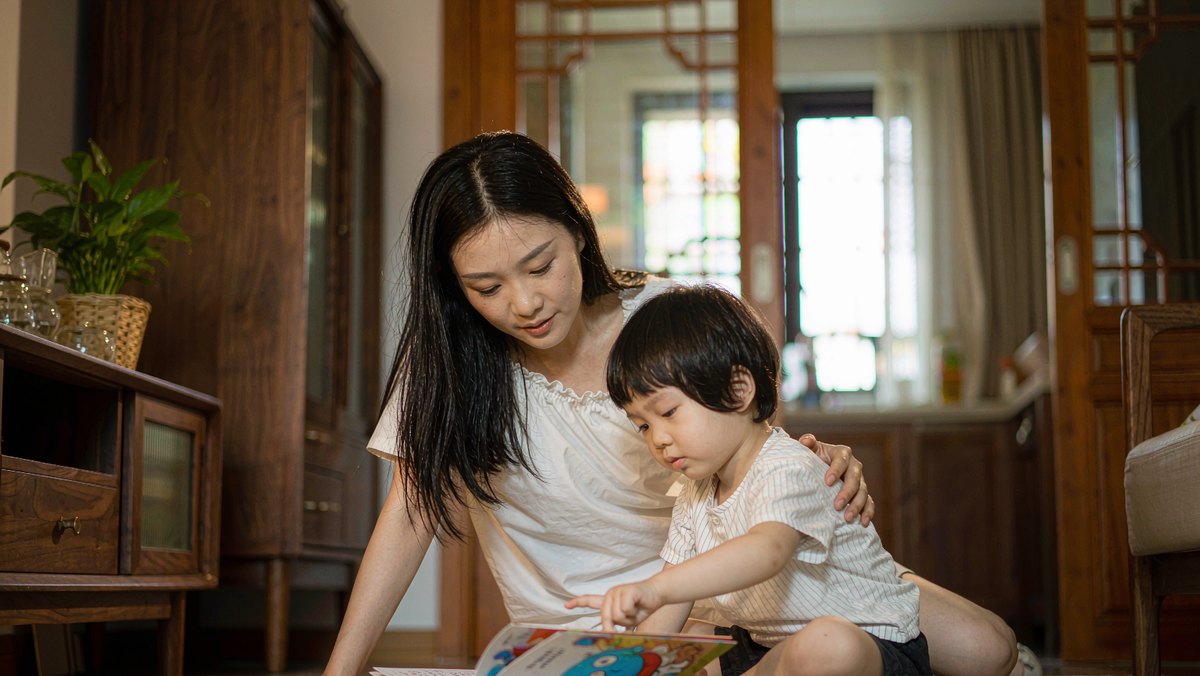 妈妈和孩子在客厅地板上共读,孩子指着书里一句话认真看
