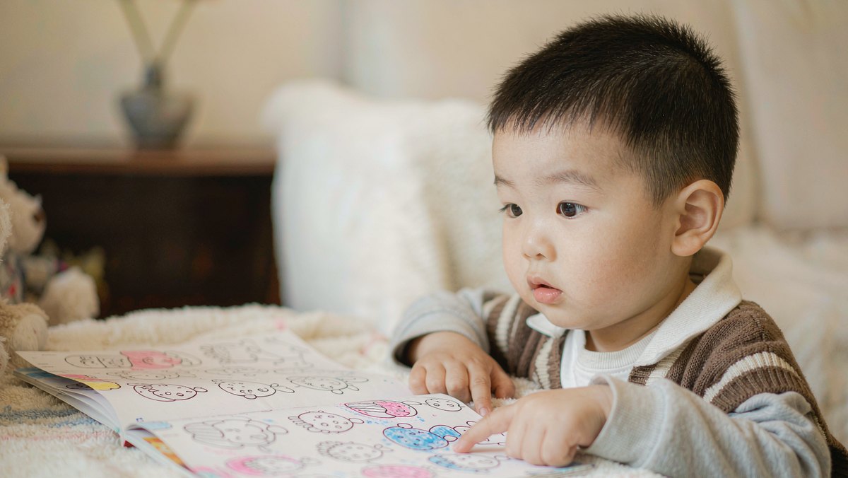孩子趴在摊开的绘本前看图