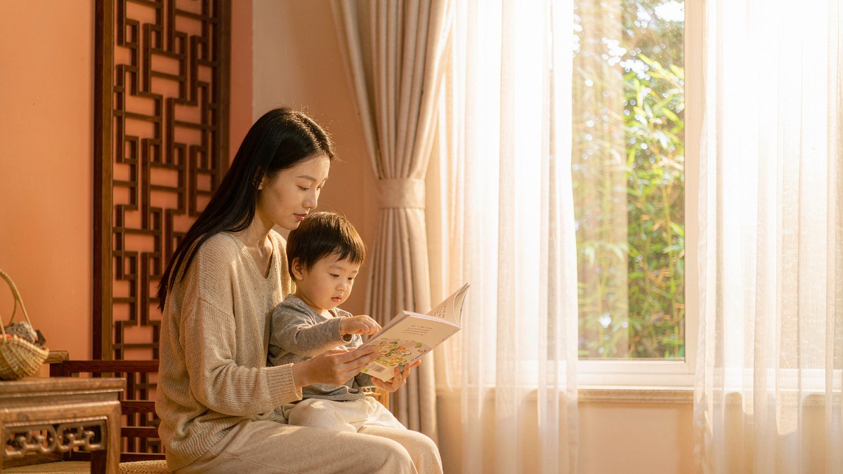 母子俩在窗边晨光里一起看书的温馨画面