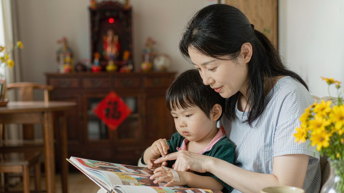 妈妈和孩子并排坐着一起研究无字书的画面细节