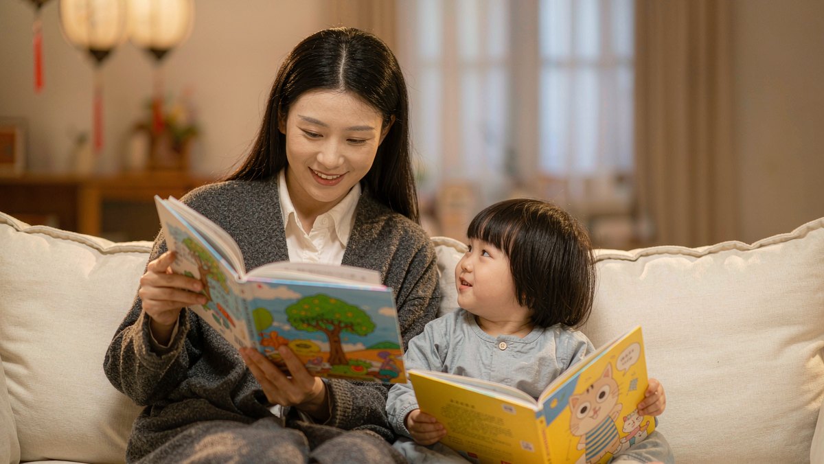 妈妈和孩子一人拿一本绘本在沙发上读